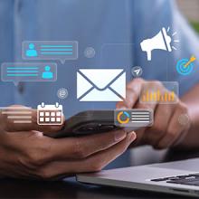 Digital email marketing and mobile communication concept entrepreneur using smartphone near laptop workspace managing online campaign messages analyzing marketing data to increase audience engagement