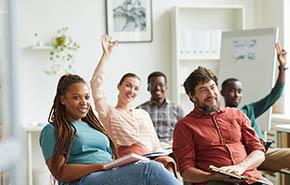 Multi-ethnic group of people raising hands while answering questions during training seminar or business conference in office