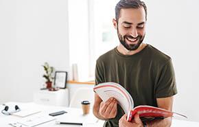 Image of caucasian happy man reading brochure and smiling 